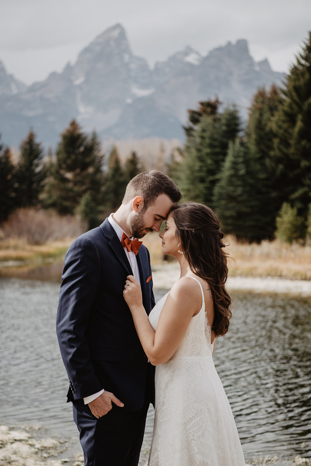 bride holding her grooms suit coat as they pull their foreheads together with the Grand Tetons in the distance