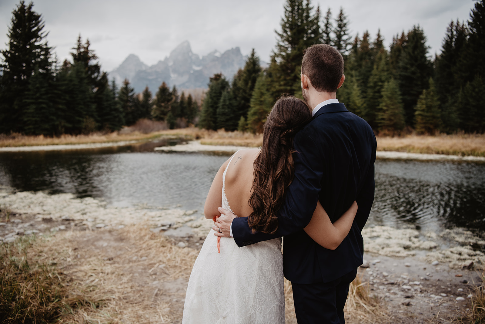 bride and groom wrapping their arms around each other as they face away from the camera towards the mountains in Jackson Hole
