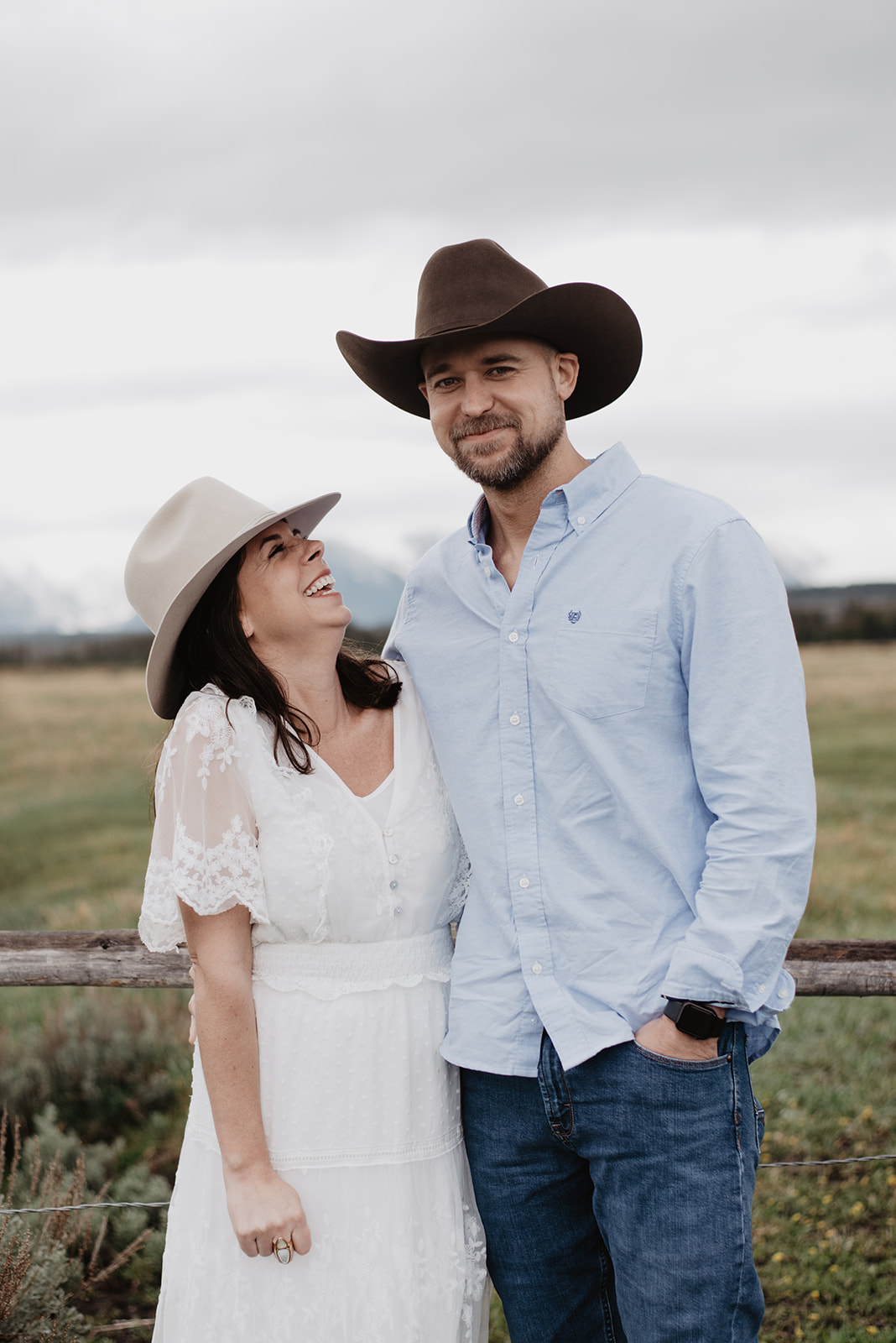 husband and wife wearing cowboy hats as the wife giggles and looks up at her husband