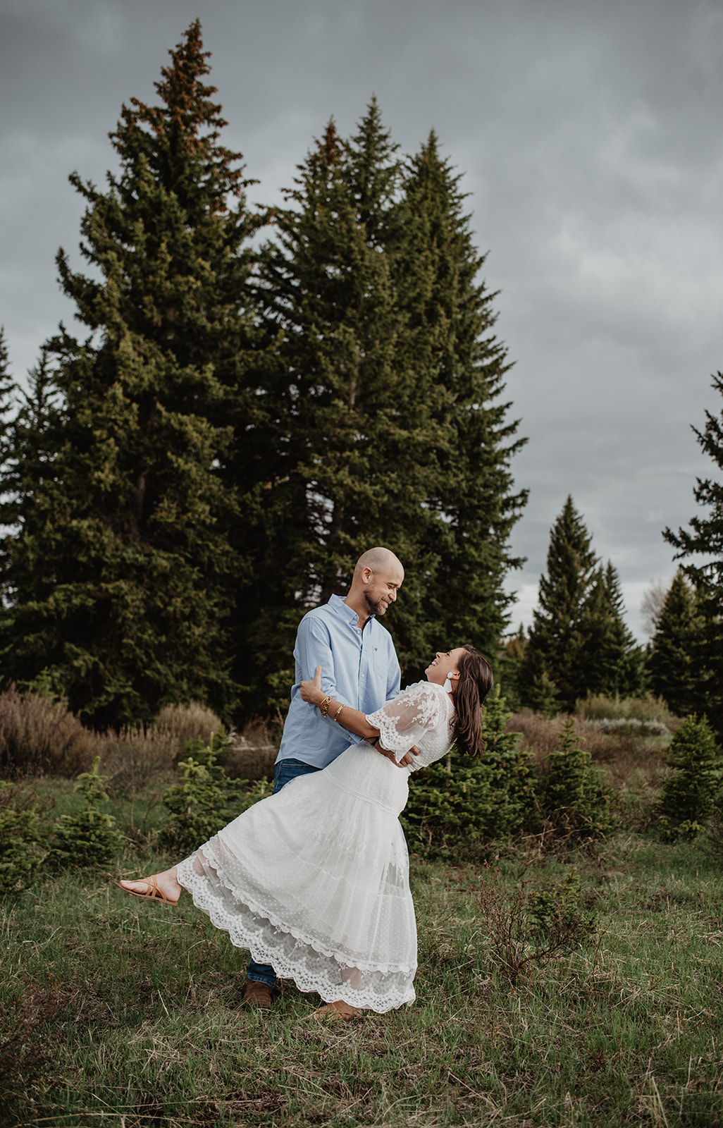 Rainy Day Photos In The Tetons anniversary session with husband dipping his wife and they dance together in front of tall pine trees