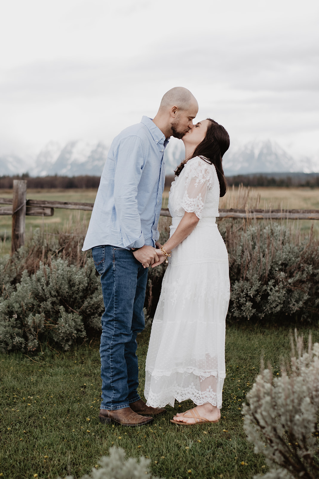 husband and wife take anniversary photos in the Tetons as they kiss and hold hands