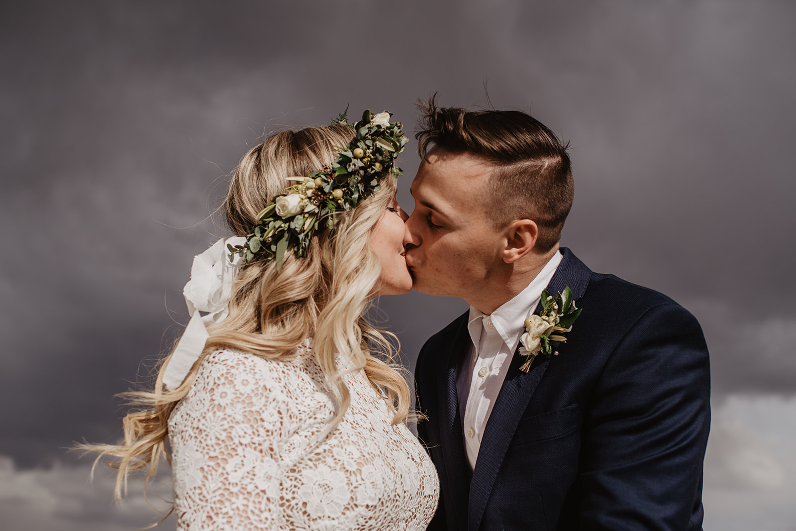 Spring elopement in the Tetons with bride and groom kissing with dark clouds behind them captured by best Grand Teton Wedding Photographer