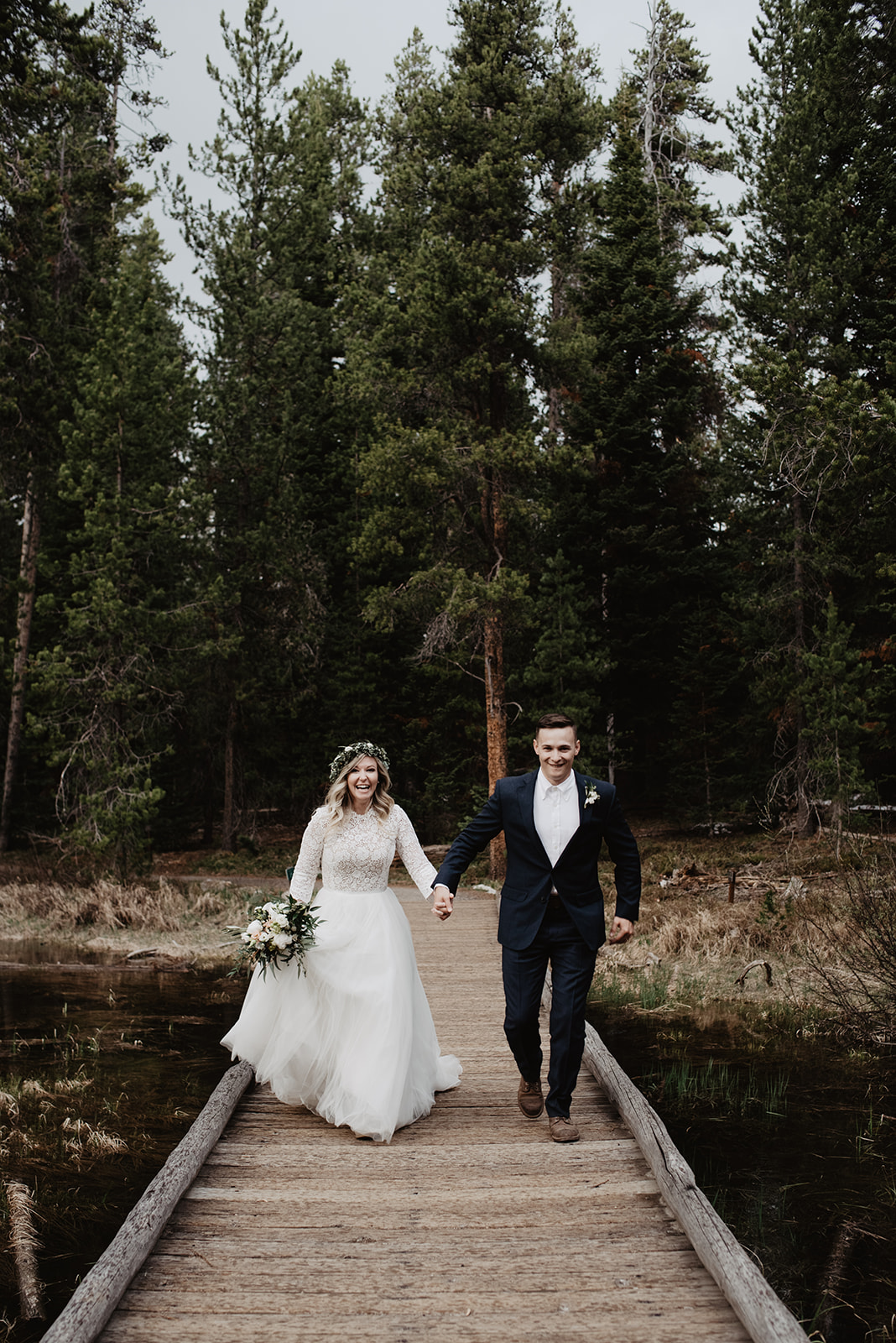 bride and groom holding hands and running down a pier on a lake in the Tetons photographed by Jackson Hole wedding photographer