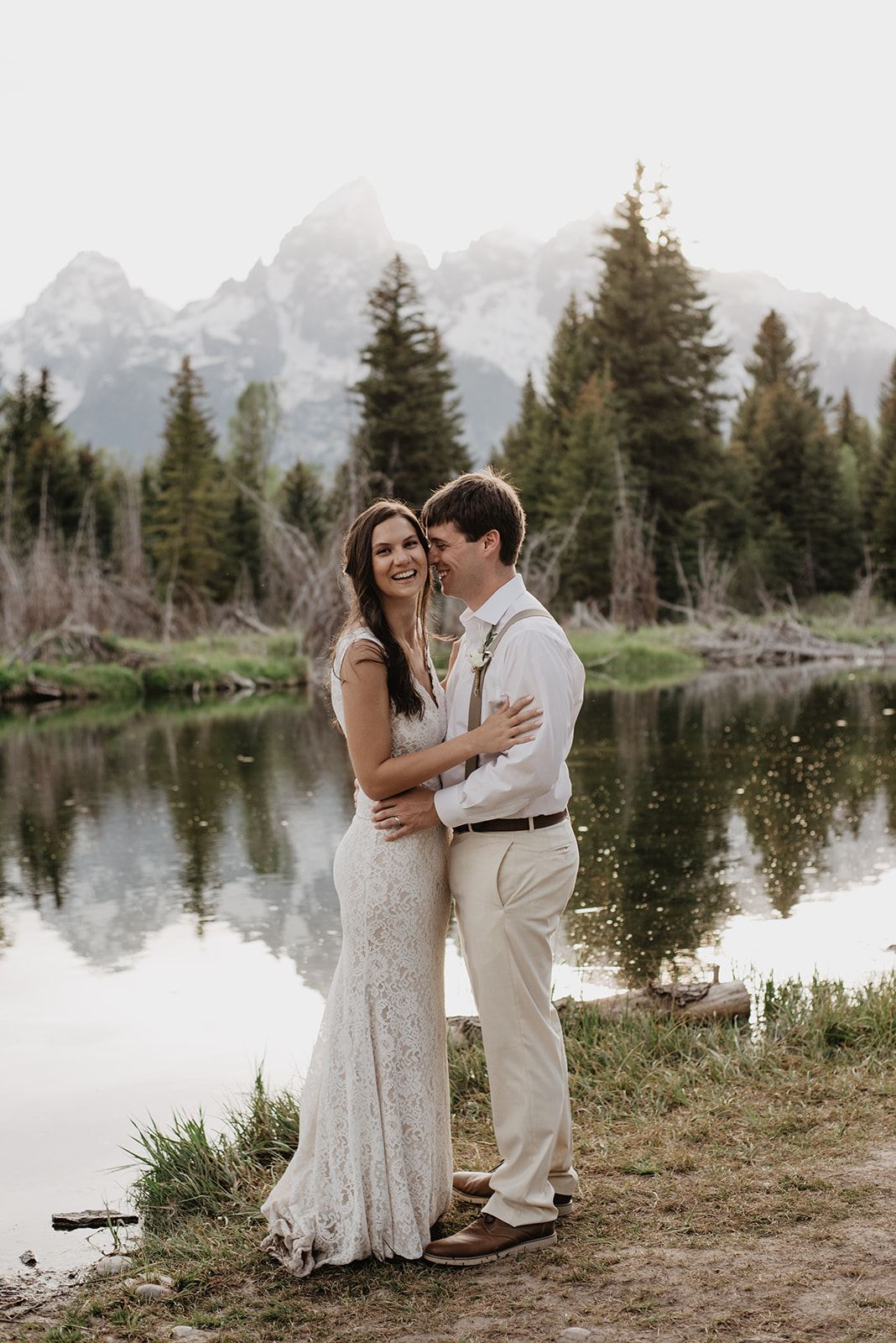 bride and groom embracing at Schwabacher Landing as the groom lays his head on his brides cheek as she smiles at the camera