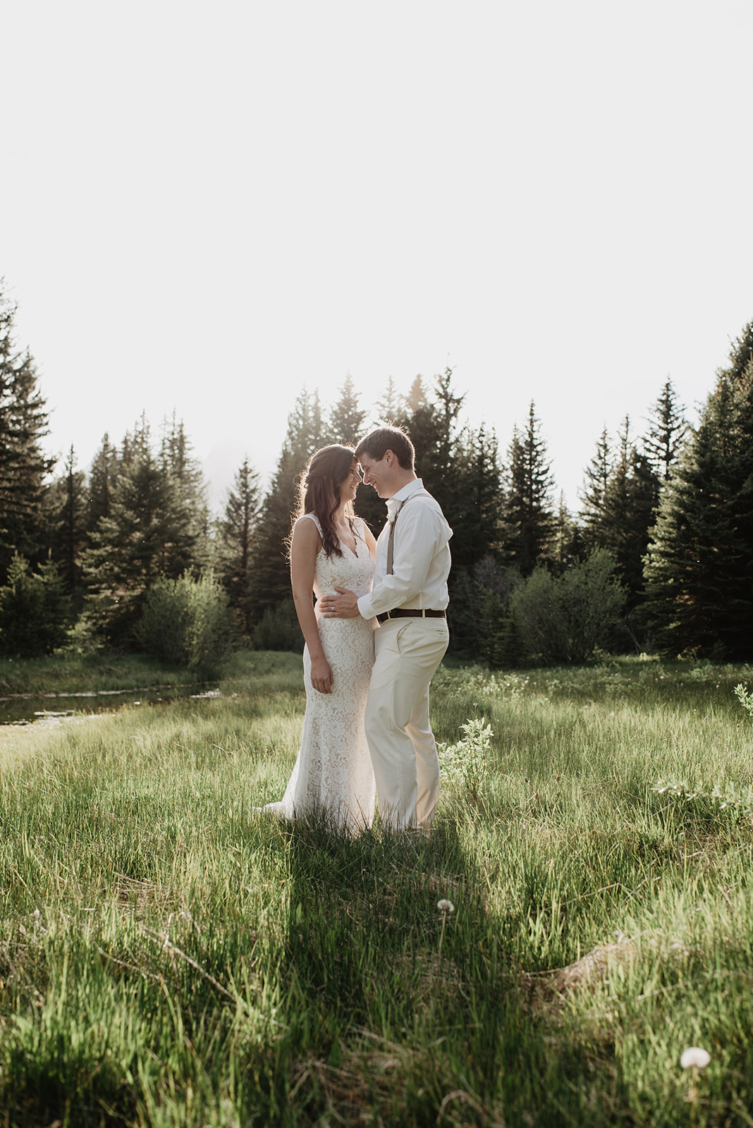 outdoor wedding photos of bride and groom holding each other in a meadow in the Grand Tetons as they rest their foreheads together romantically and the bride wears a lace wedding gown