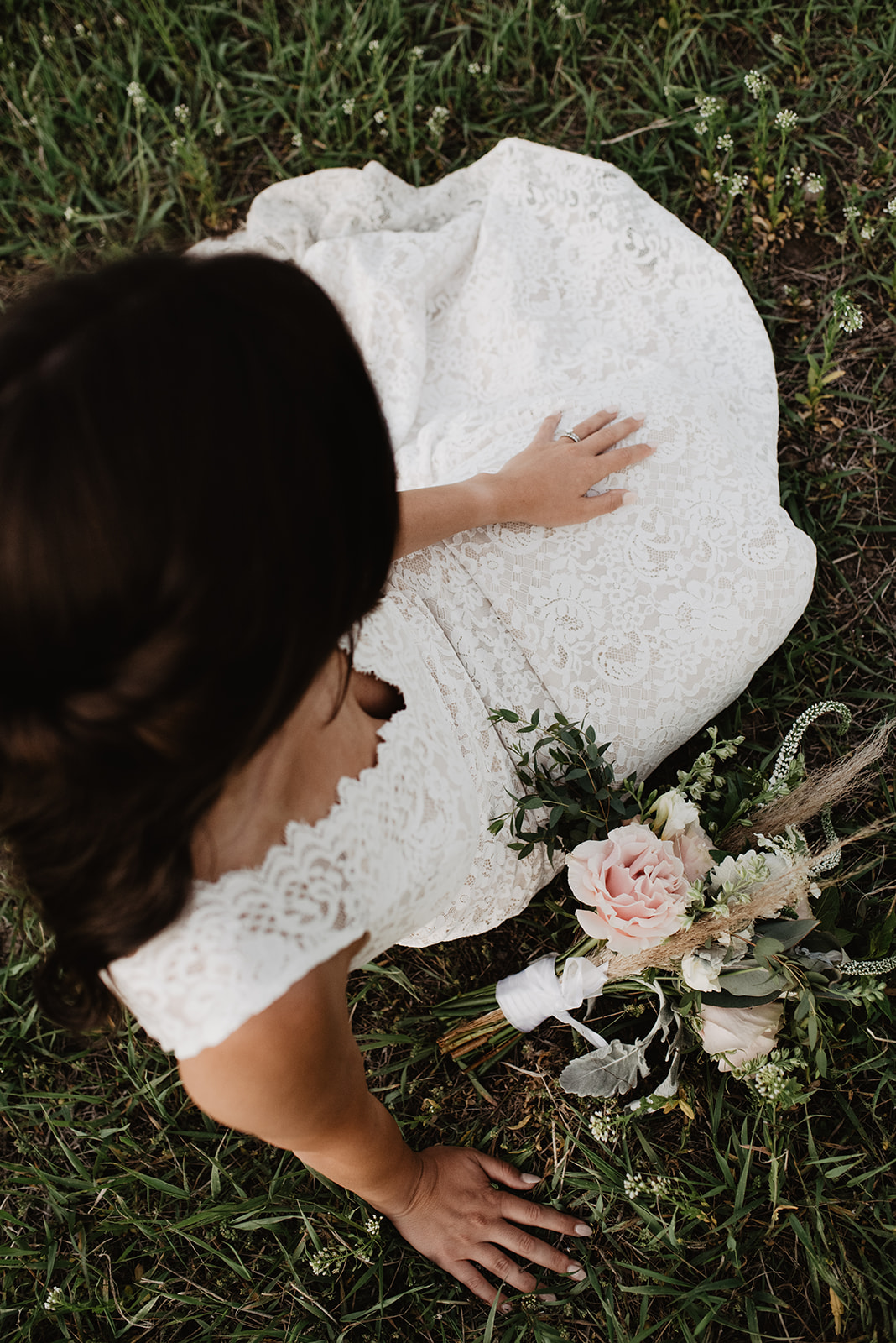bride in a lace wedding dress sitting on the ground in the Tetons with her floral wedding bouquet 