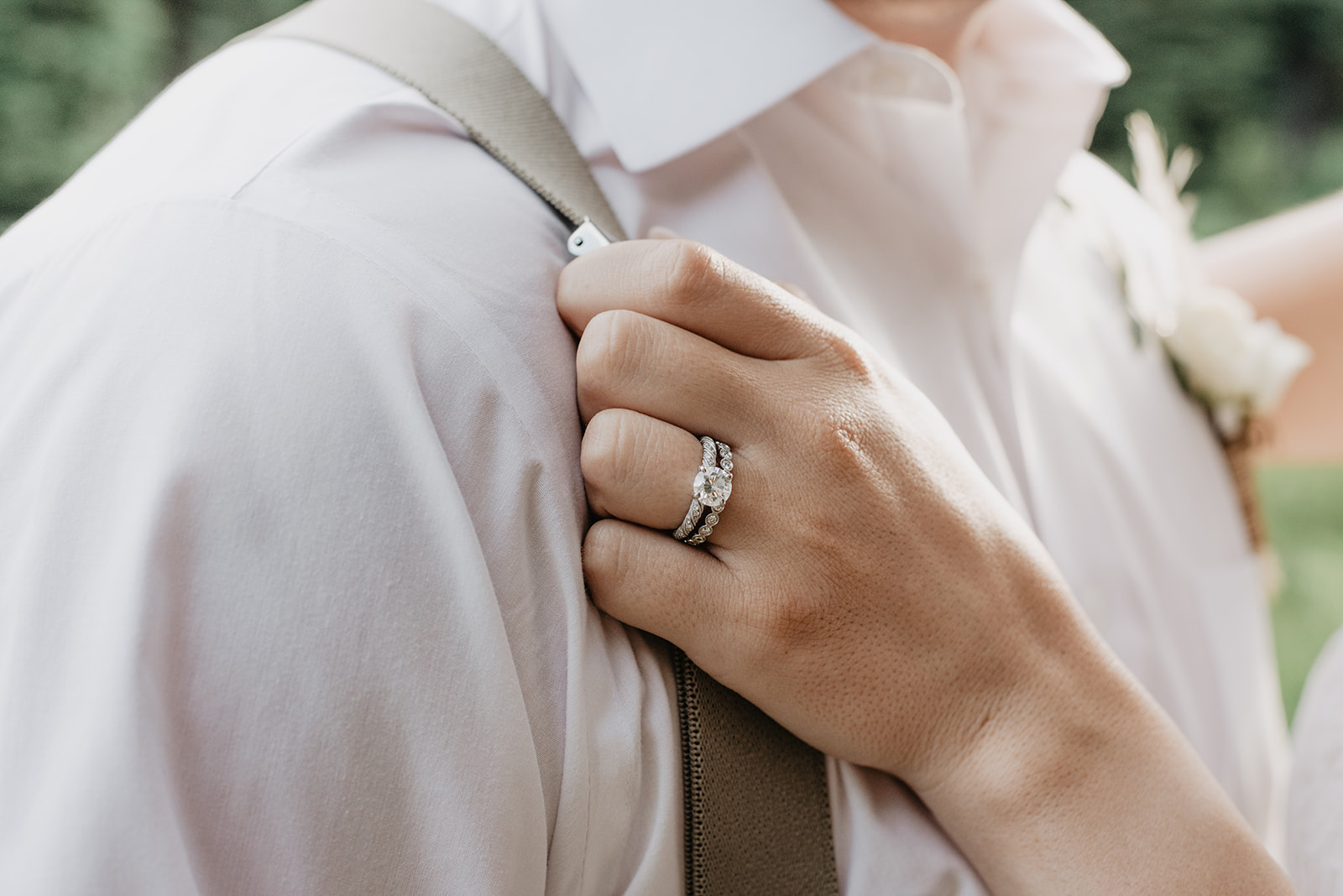 bride holding her grooms suspender for a detail shot of her wedding and engagement rings 