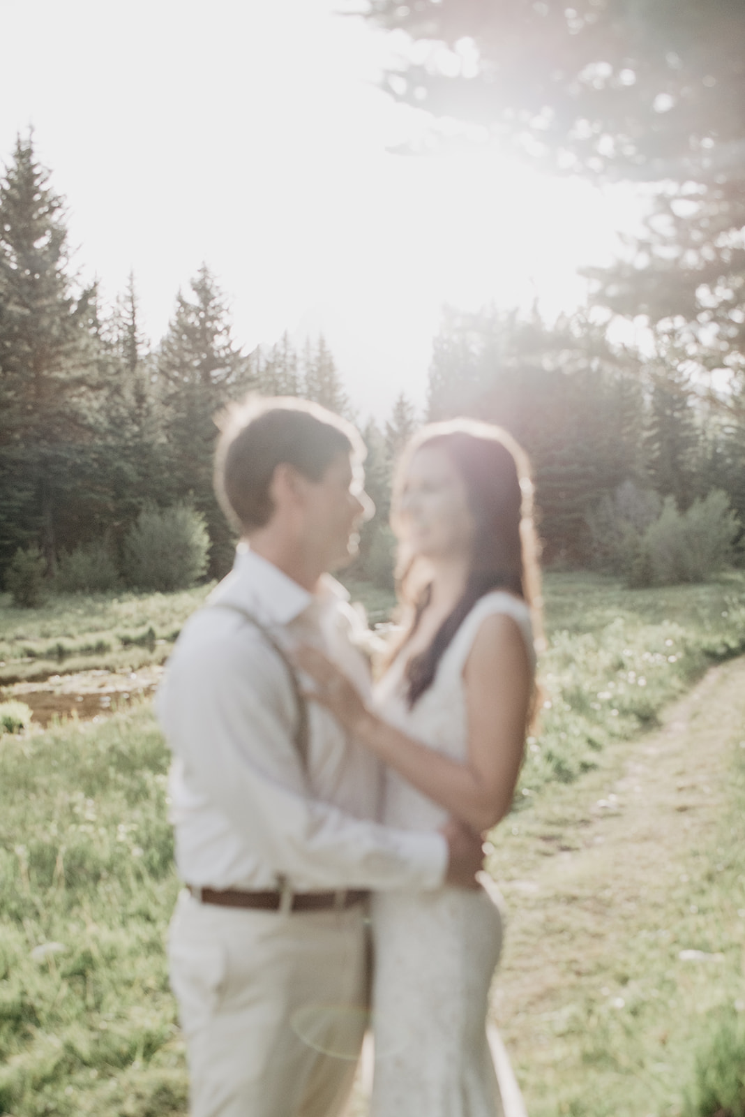 out of focus wedding photog of bride and groom in the sunshine while standing in a meadow in the Grand Tetons for a beautiful wedding portrait