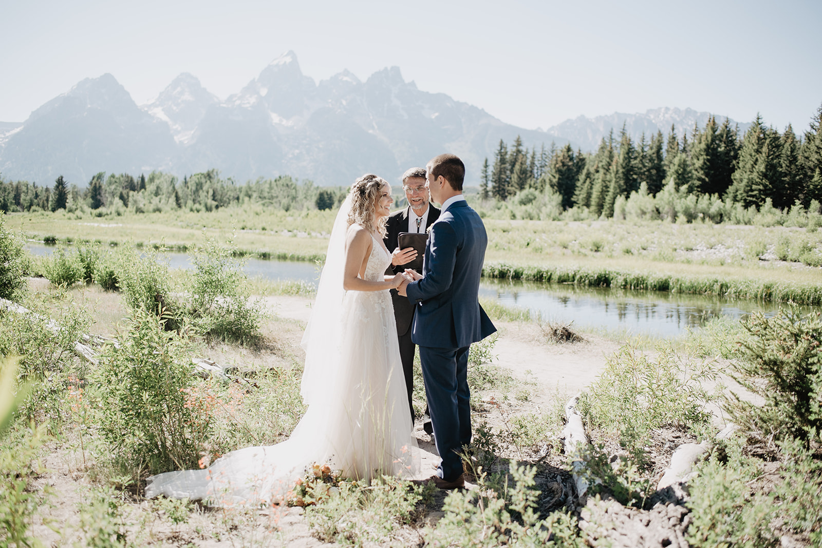Grand Teton summer elopement wedding ceremony with bride and groom holding hands while their officiant marries them with the Tetons mountains behind them