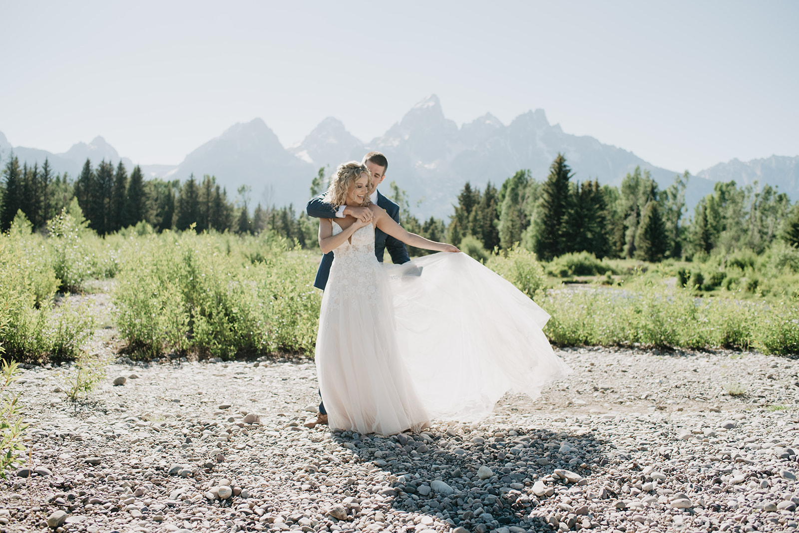 bride and groom dancing at Schwabacher Landing for their Grand Teton summer elopement with the groom standing behind the bride as they sway together 