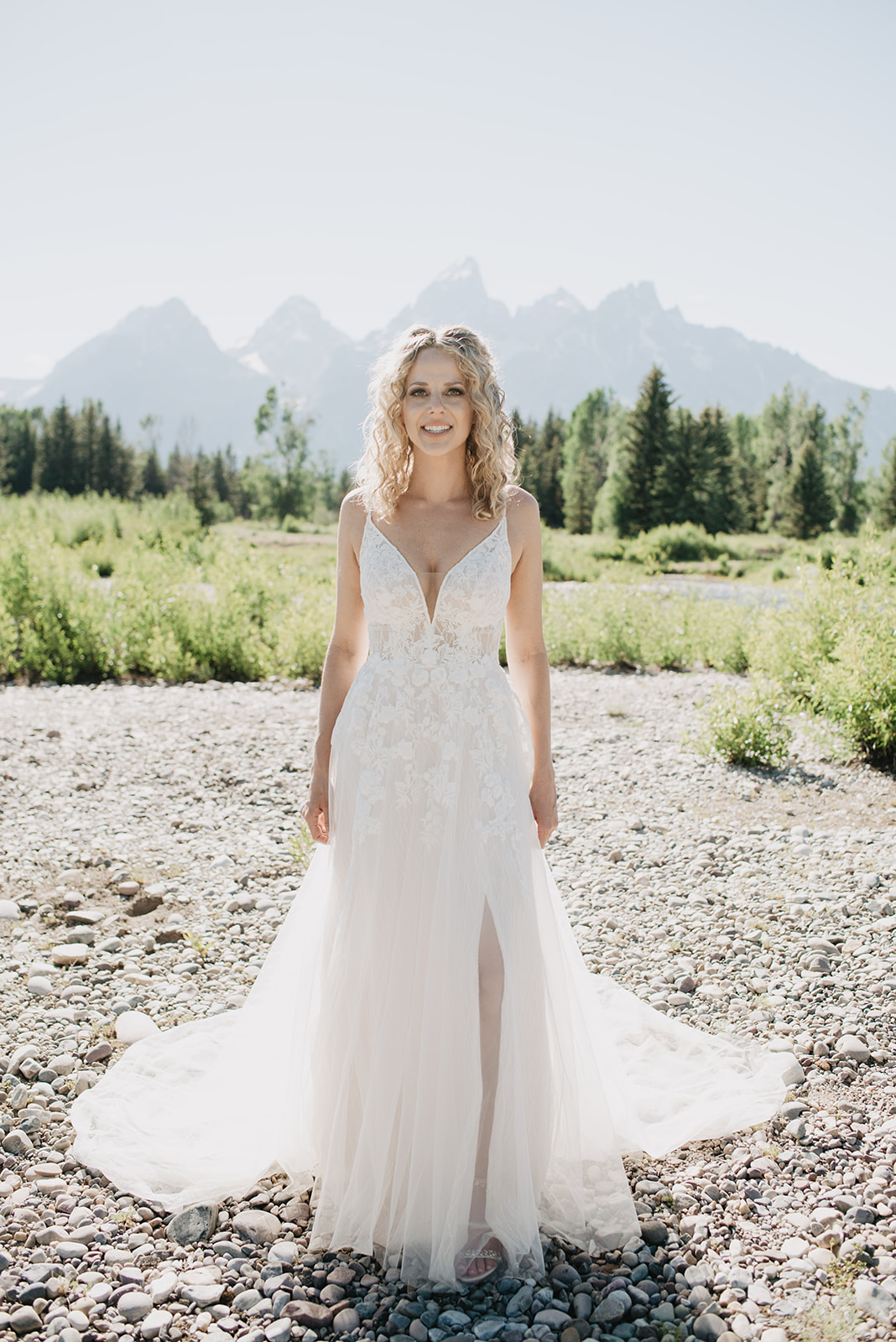 bride in her lace and tulle wedding dress standing on a rock path in the Tetons with the mountains in the distance for her bridal portraits with Jackson Hole photographers 