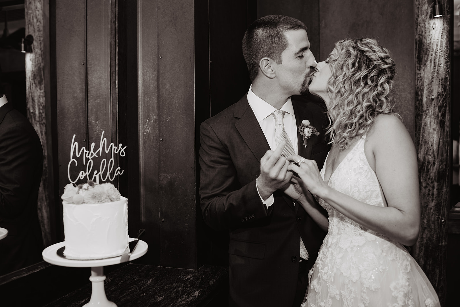 black and white wedding photo captured by best Jackson Hole wedding photographer with bride and groom kissing next to their wedding cake during their celebratory wedding dinner