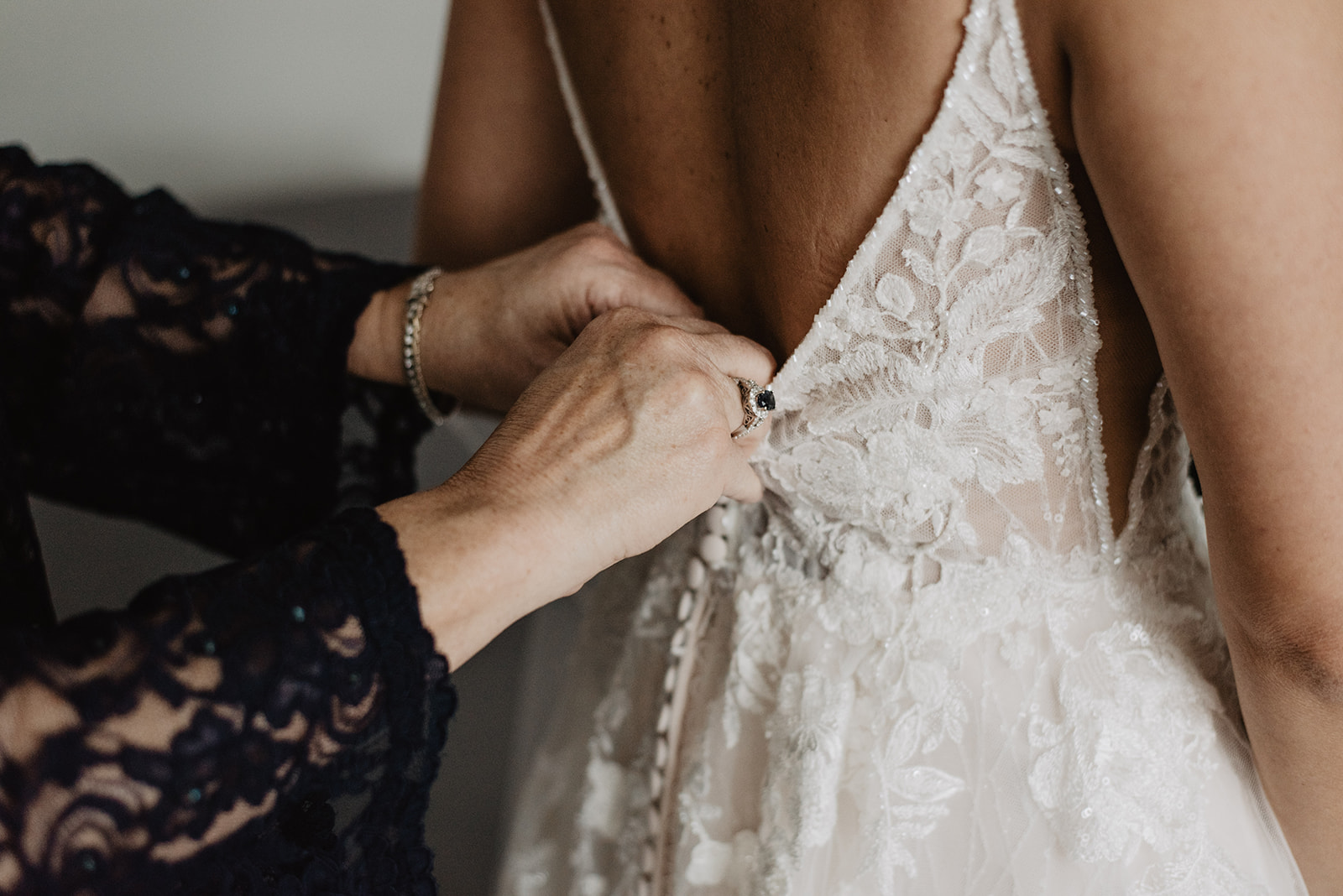 detail shot of brides mother buttoning up the back of her dress as the bride gets ready for her wedding ceremony