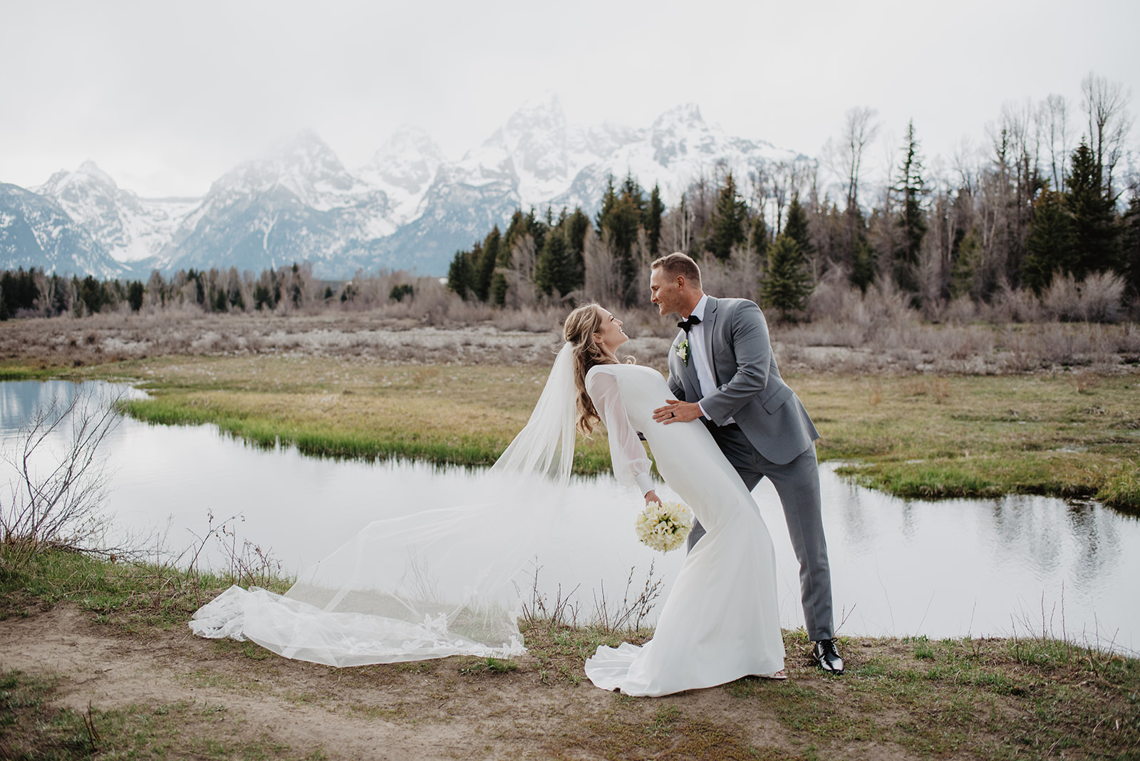 Grand Teton wedding photos with groom dipping his bride back as her veil flows int he wind behind her with the mountains in the distance