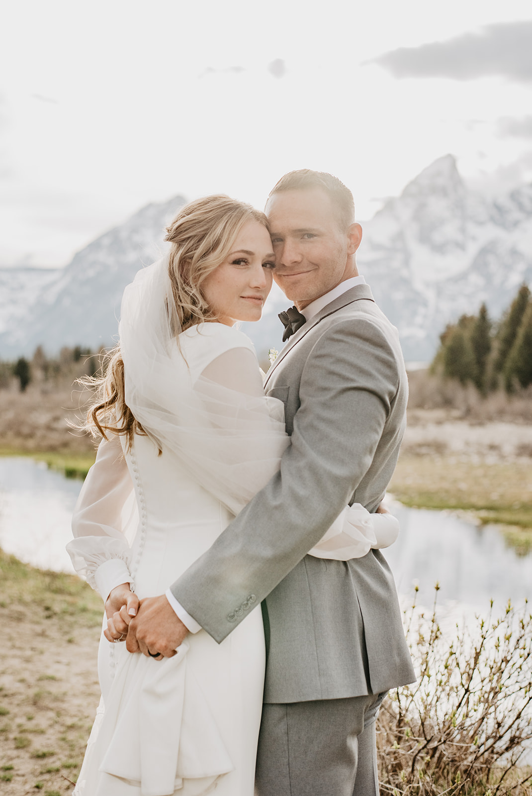 outdoor wedding photos in the Grand Tetons with bride and groom holding each other and looking over their shoulders to the camera