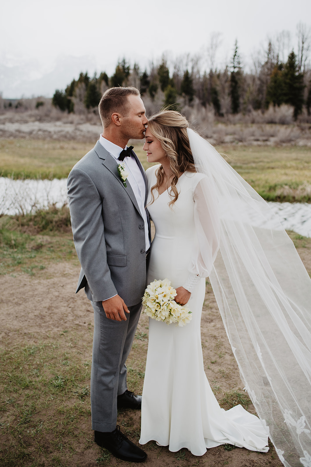 Grand Tetons wedding photo with bride and groom holding hands as the groom kisses the brides forehead