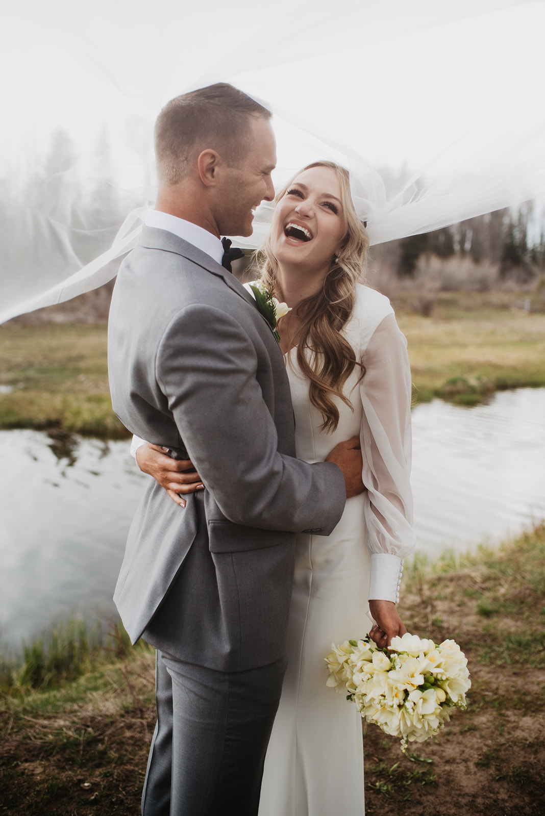 Grand Tetons wedding photos with bride laughing as her veil falls over both her and her grooms head during their outdoor photoshoot