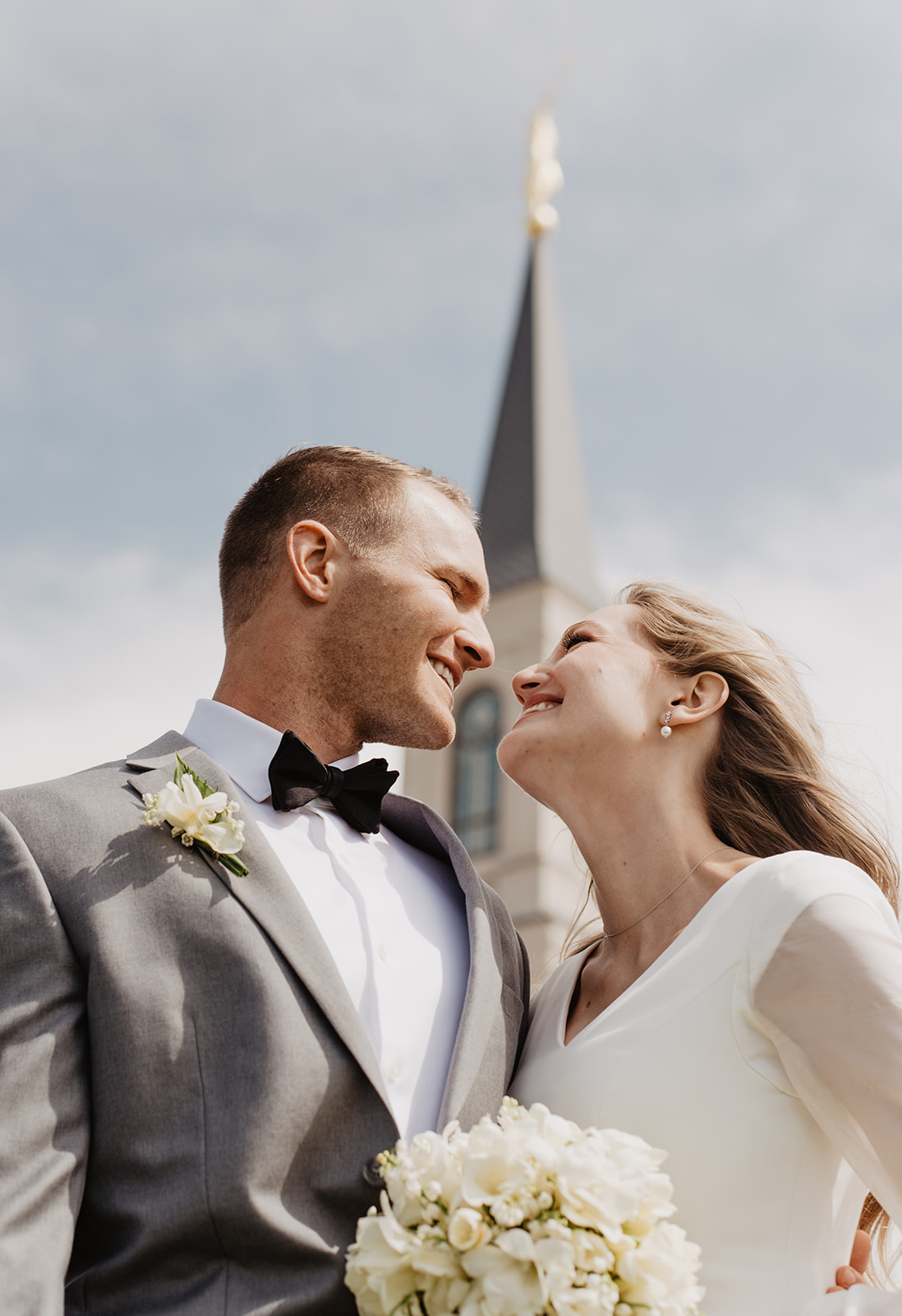 bride and groom outside of the Afton lds Temple in Wyoming smiling at each other with the steeple of the temple behind them