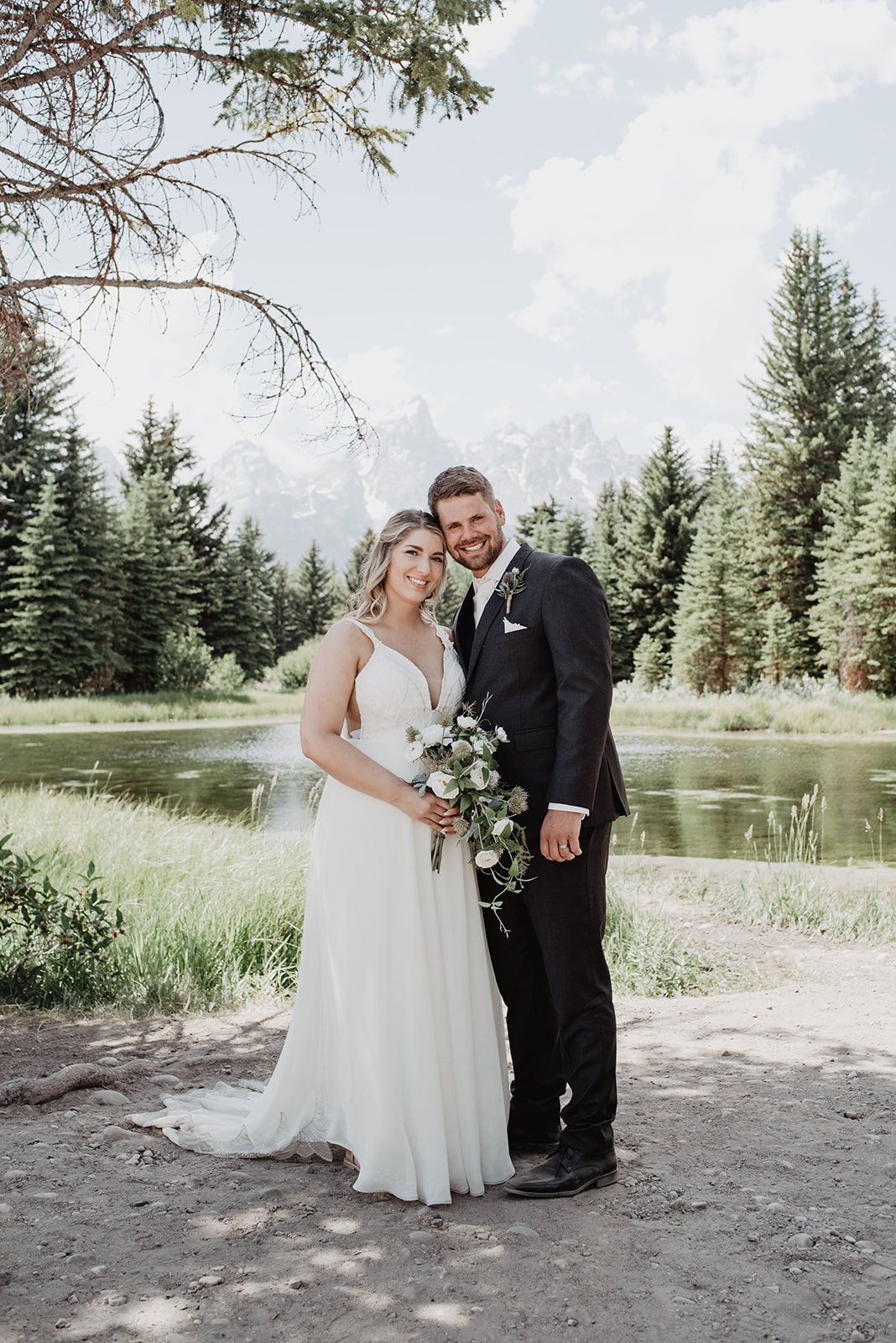 bride and groom standing together in front of a river with the Grand Tetons mountains behind them