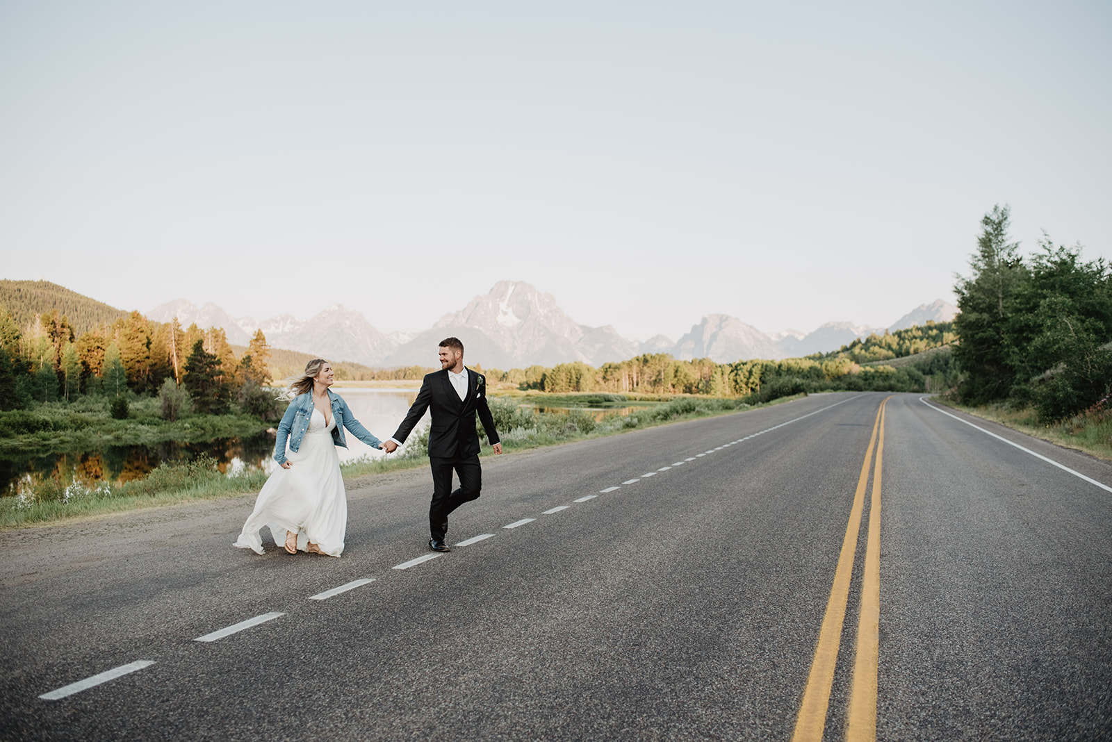 adventure wedding photographer captures bride adn groom holding hands and running across the road in Jackson Hole