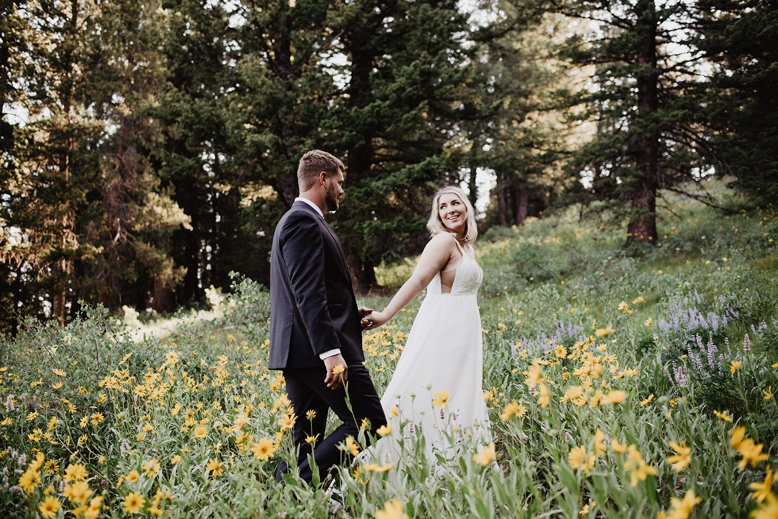 bride holding her grooms hand as she leads him through a meadow in Jackson Hole for their destination elopement