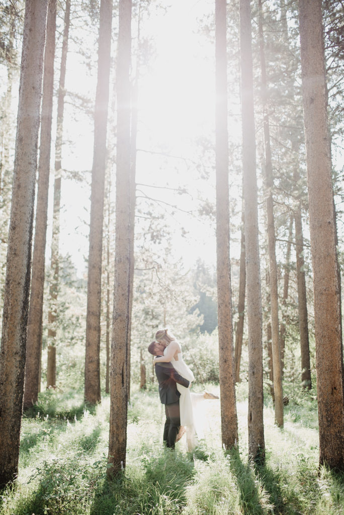 woodland wedding photo with groom holding his bride as the sun shines through the trees overhead