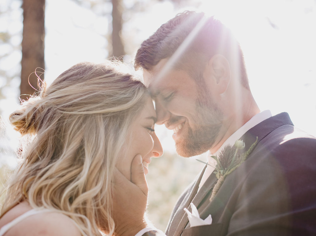 sun shining over bride and groom as groom embraces brides face and sets his forehead on top of her head