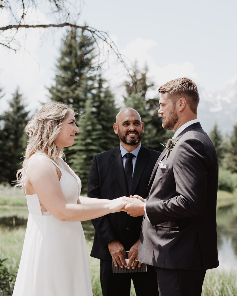 bride and groom hodling hands and saying their vows for their Grand Teton wedding with their officiant next to Snake River during their summer wedding captured by  Jackson Hole photographers