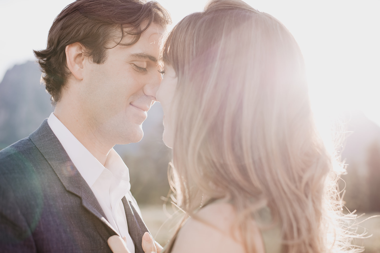man and woman embracing close as they smile and the sun shine behind them gleaming through the couple