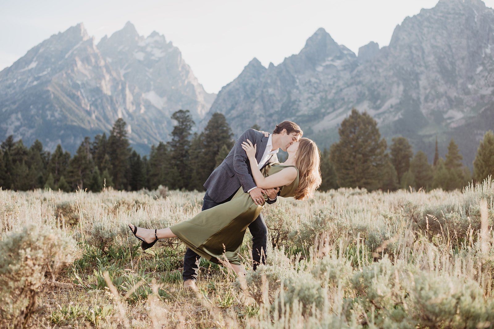 man dipping woman in an olive green dress as they dance together in a meadow in the Grand Tetons