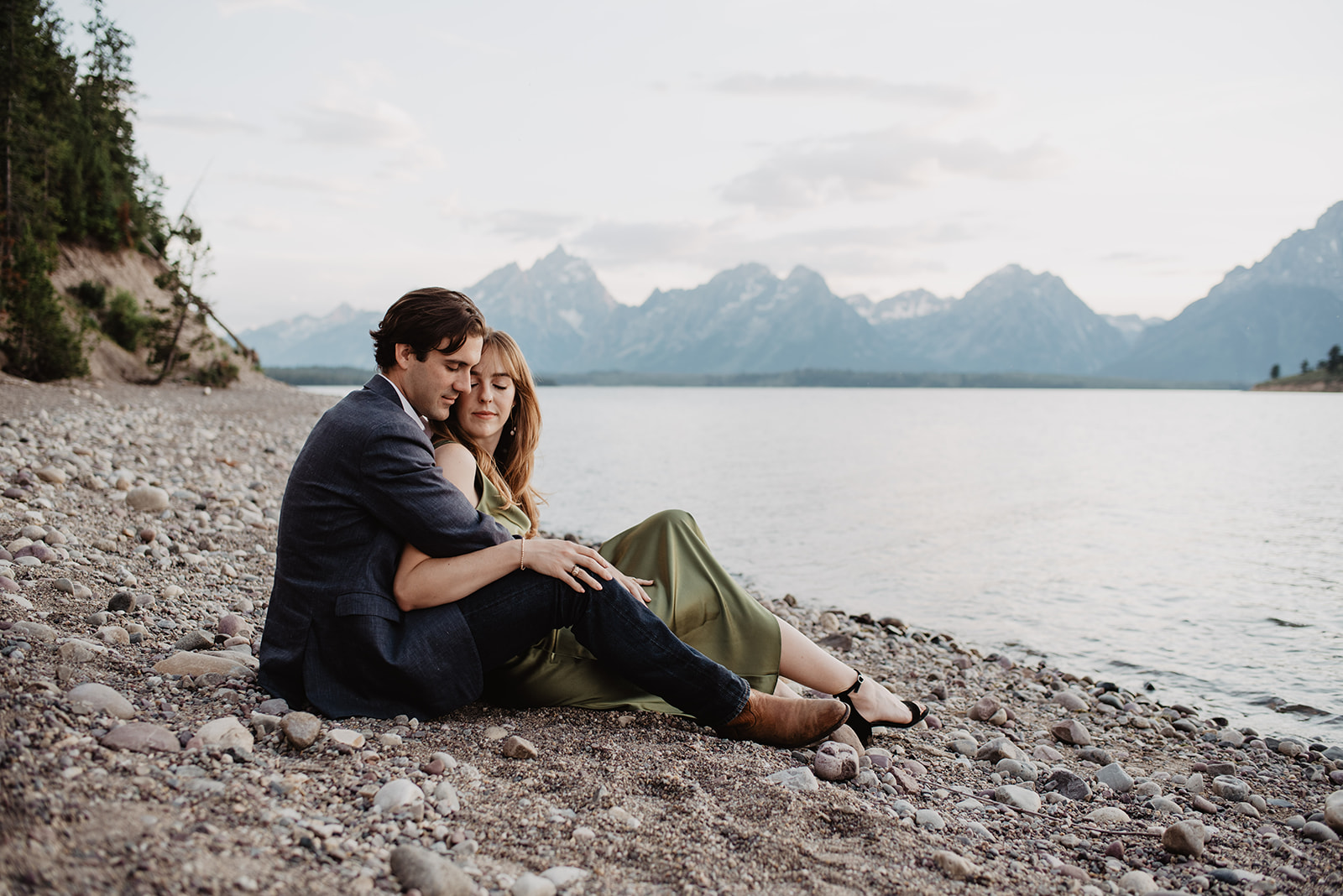 man and woman sitting together on a beach next to a lake in the Grand Tetons