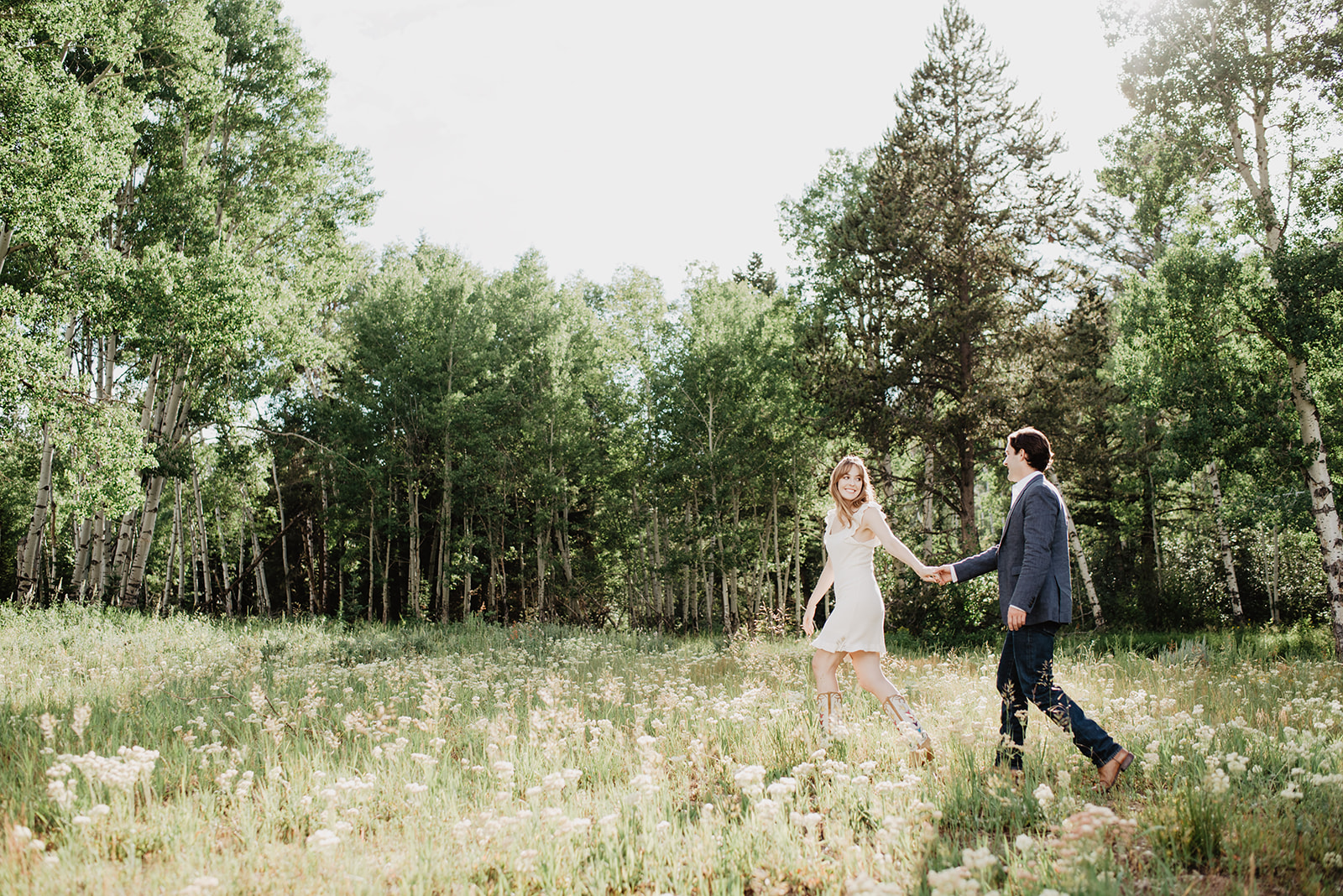 woman holding mans hand and leading him through a meadow in Grand Teton National Park for their summer engagement session