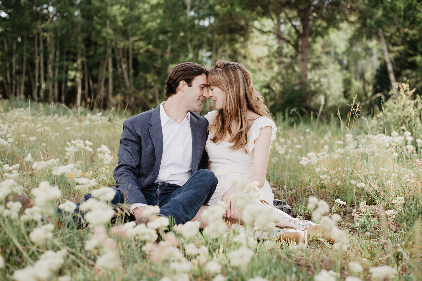 man and woman sitting together in a wildflower feild in Jackson Hole as they place their foreheads together and gently smile