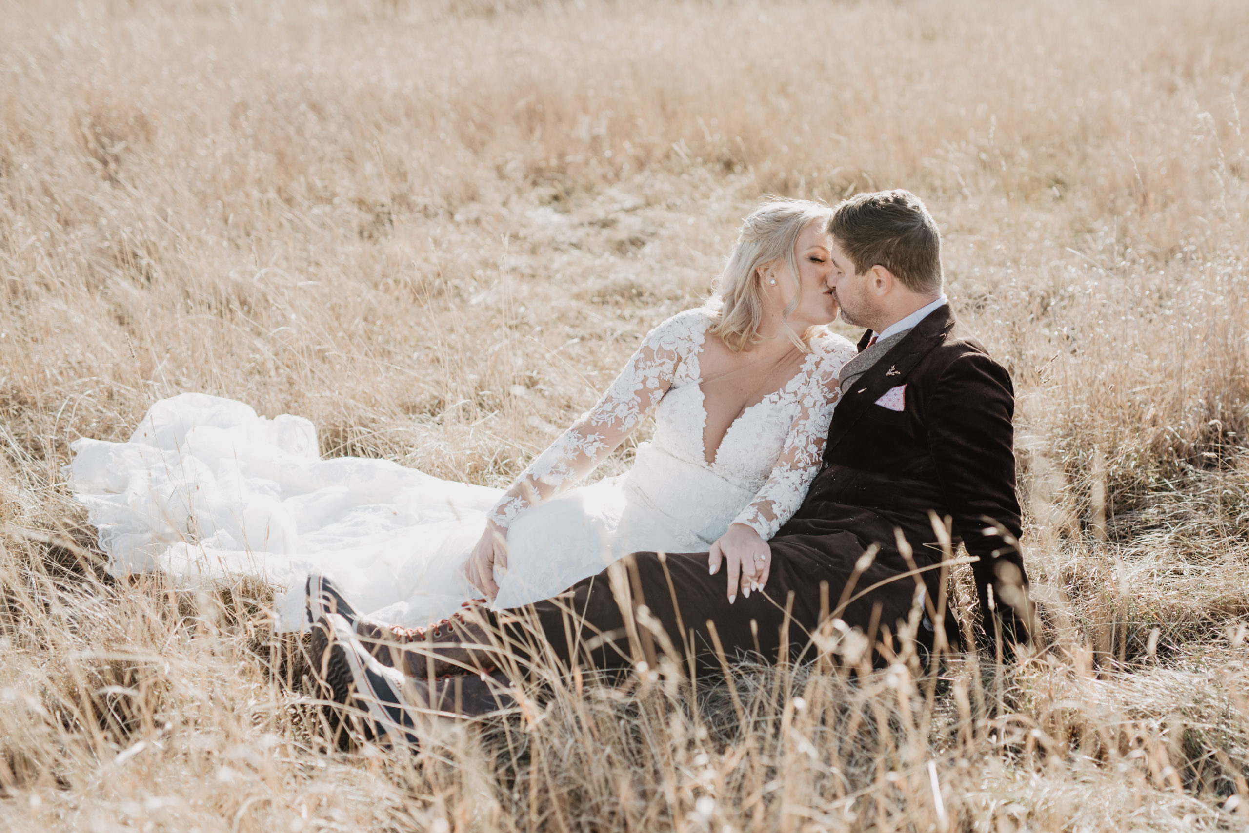 Grand Teton National Park wedding photographer captures bride and groom sitting in a golden field in the Tetons as they kiss for their fall wedding