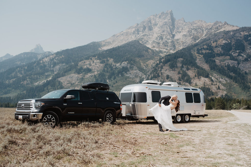 bride and groom standing in front of their airstream on their wedding day in the Teton mountains as the groom dips the bride back and kisses her 