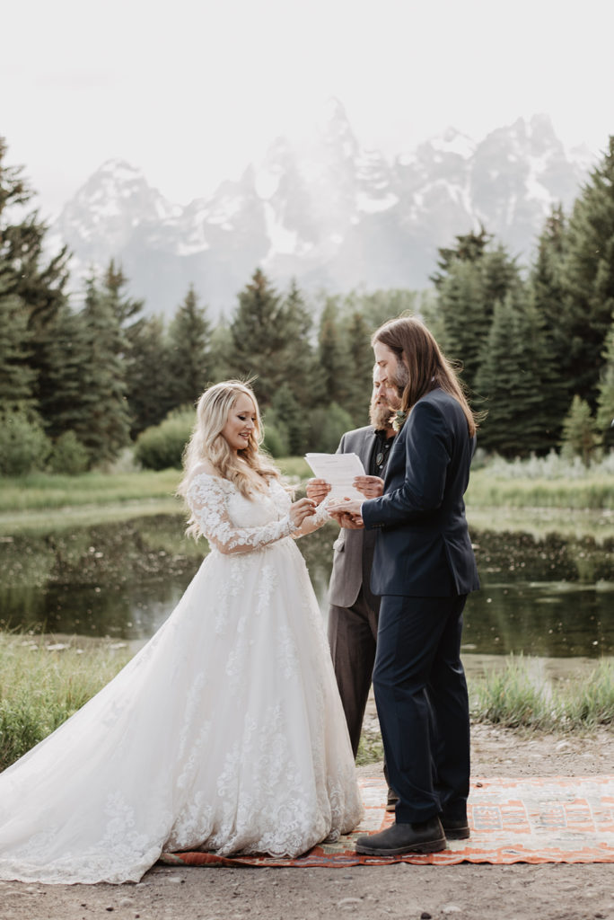 Jackson Hole wedding ceremony near the water of a river at Schwabacher Landing with bride adn groom sharing their vows together 