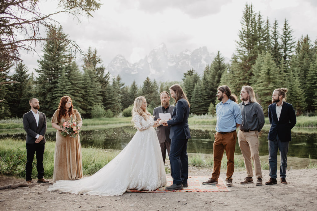 jackson hole wedding photographer captures bride and groom holding hands during their wedding ceremony in the grand tetons surrounded by friends 