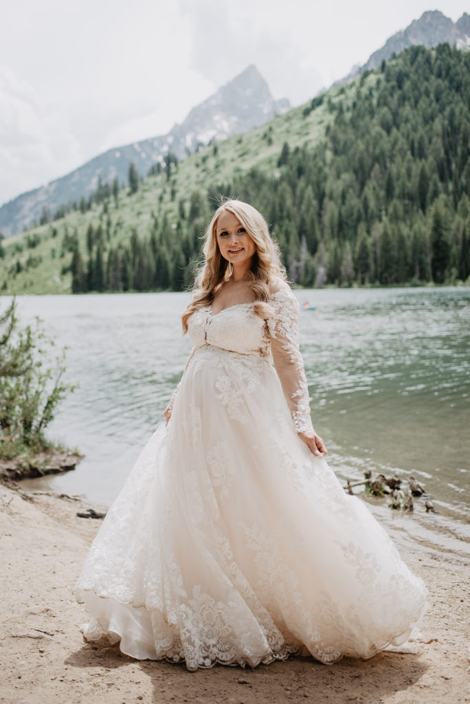 bride standing on a lake in the Grand Tetons wearing a tulle and lace wedding dress while dancing for her Grand Teton elopement