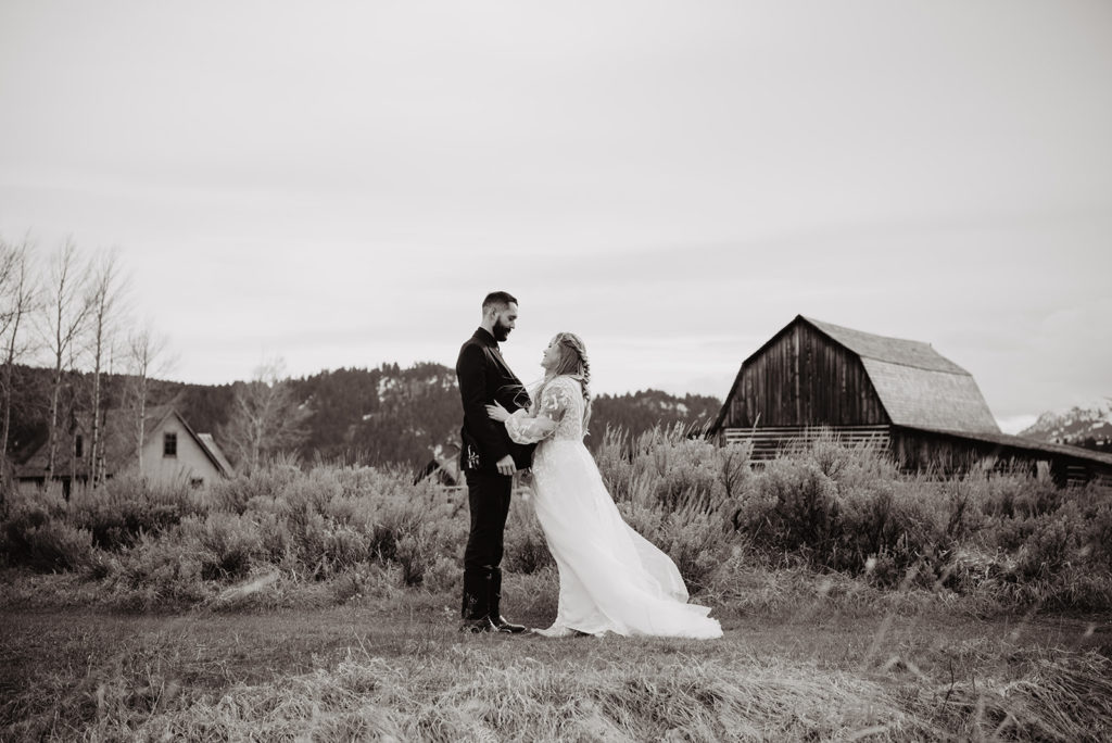 outdoor barn wedding in the Tetons photographed by Jackson Hole photographers with bride and groom embracing outside of a barn in the mountains 