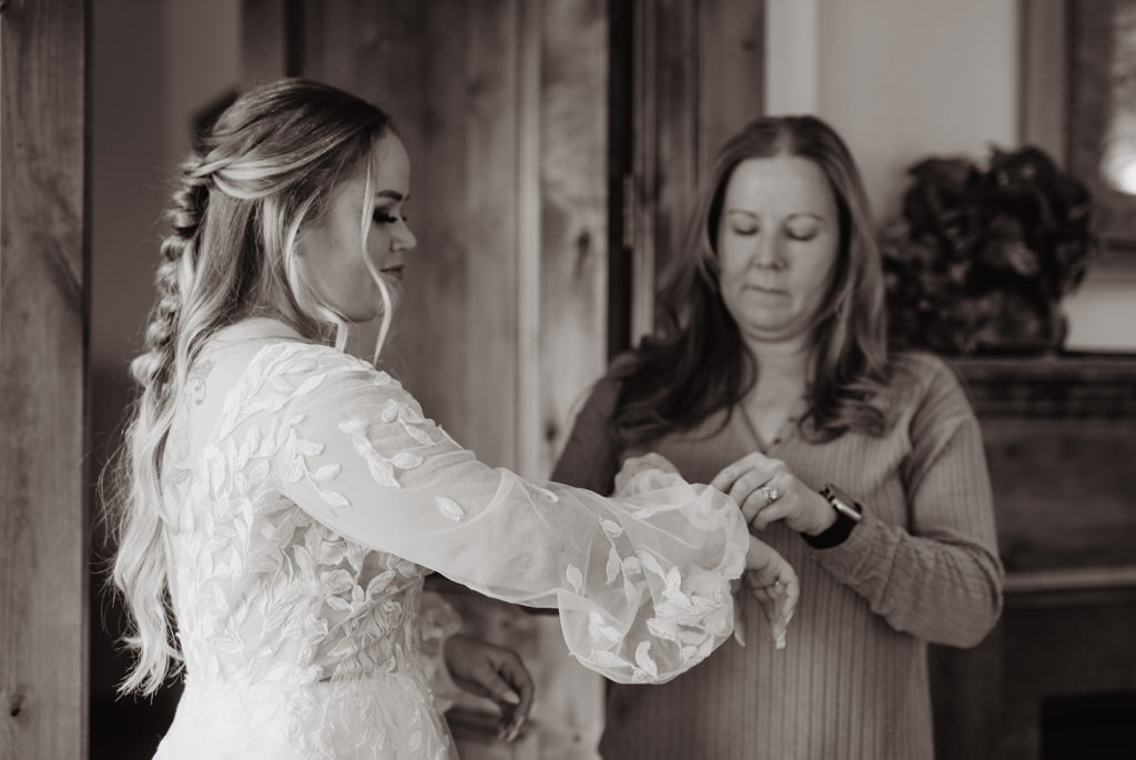 mother of the bride helps the bride button the long sleeves on her lace wedding dress for her getting ready photos with Jackson Hole wedding photographer 