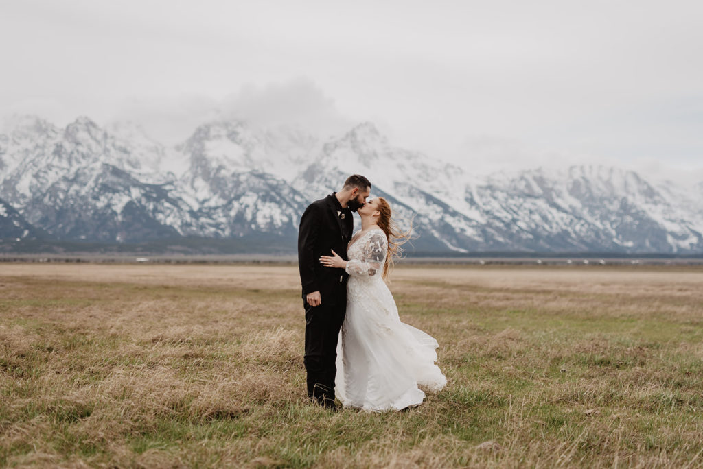 bride and groom kissing in a field with the Tetons behind them as a fog rolls in taken by Jackson Hole photographers