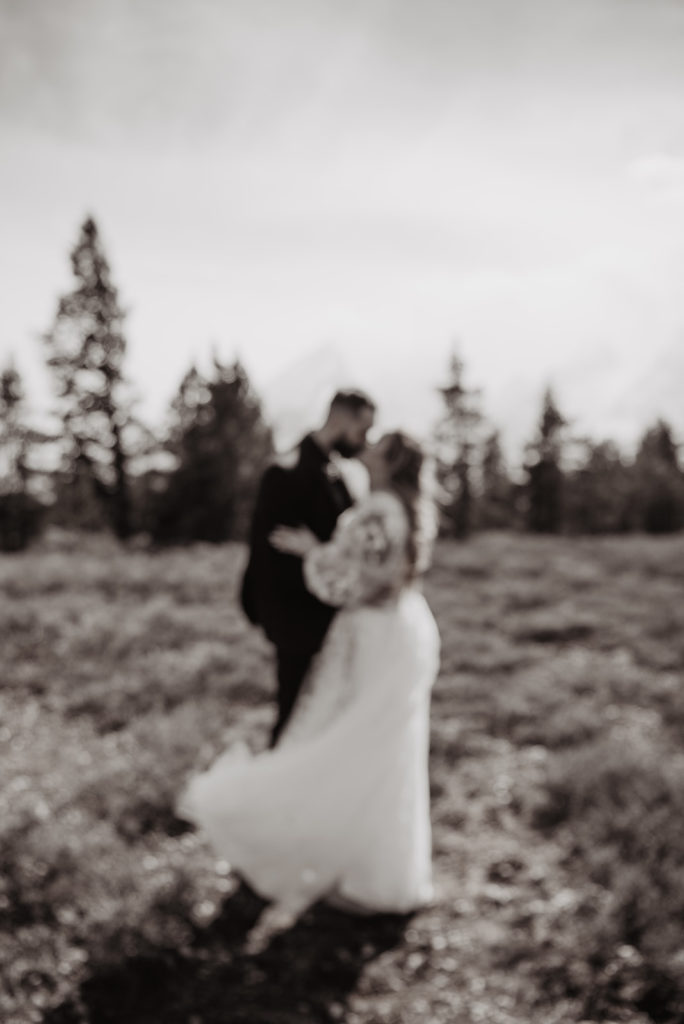 Jackson Hole wedding in the woods with bride adn groom holding each other and looking at the mountains in the distance 