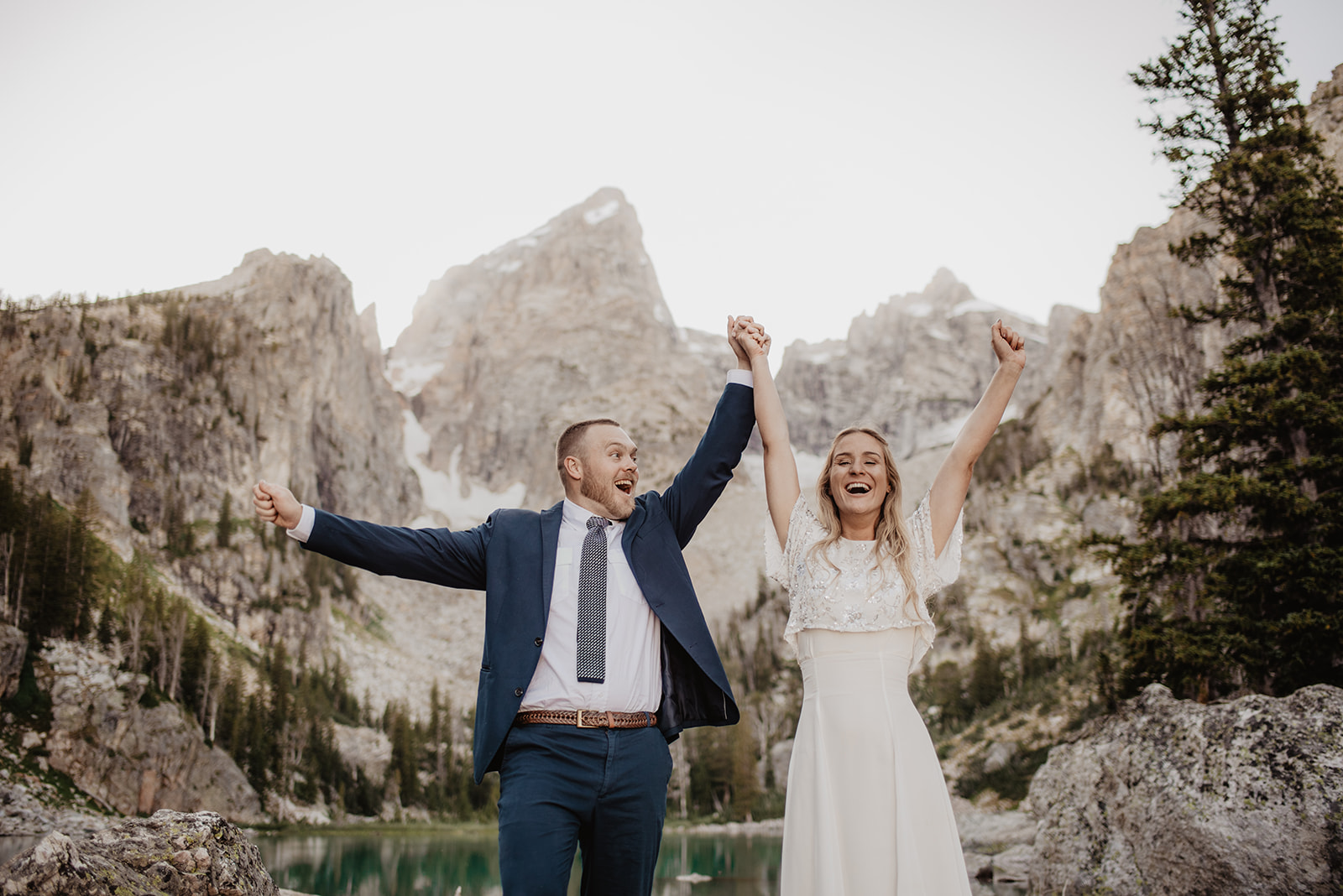 outdoor wedding photos with Jackson Hole wedding photographer with bride and groom holding hands and cheering in celebration with the Tetons behind the couples