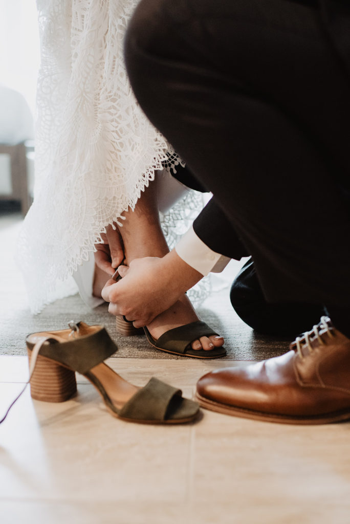 groom helping his bride put on her wedding shoes the morning of their elopement