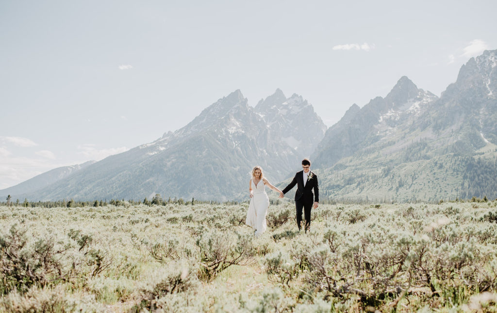 bride and groom holding hands and walking through a valley with the Tetons in the distance taken by jackson hole wedding photographers