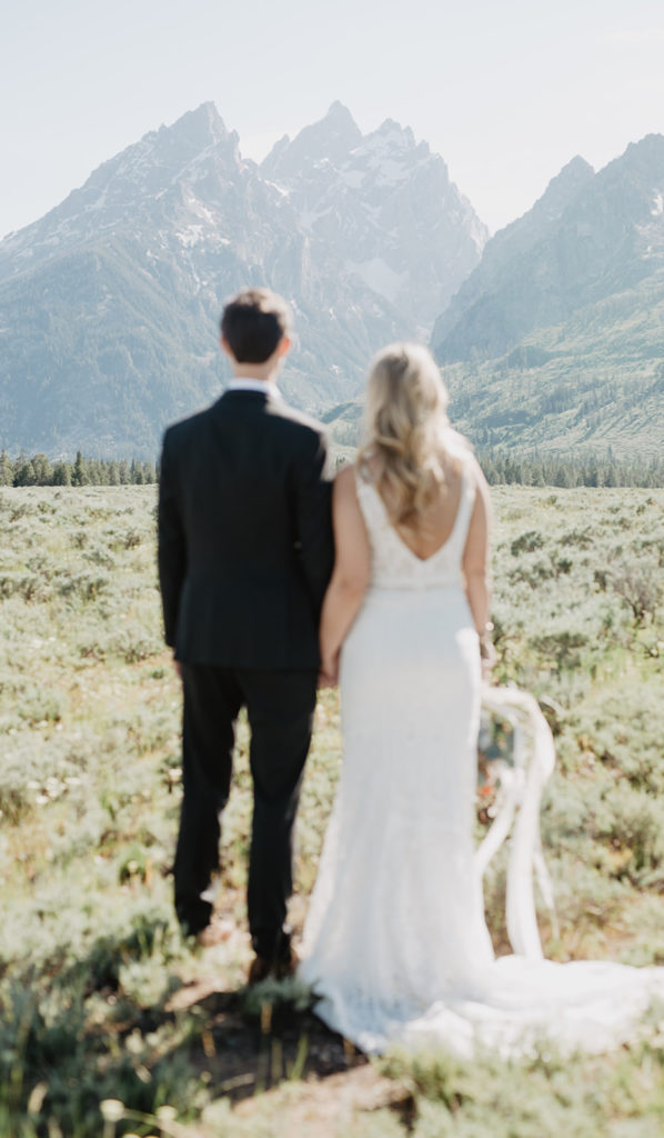 grand teton wedding with bride and groom holding hands and looking to the mountains at sunset for their wedding portraits by jackson hole photographers