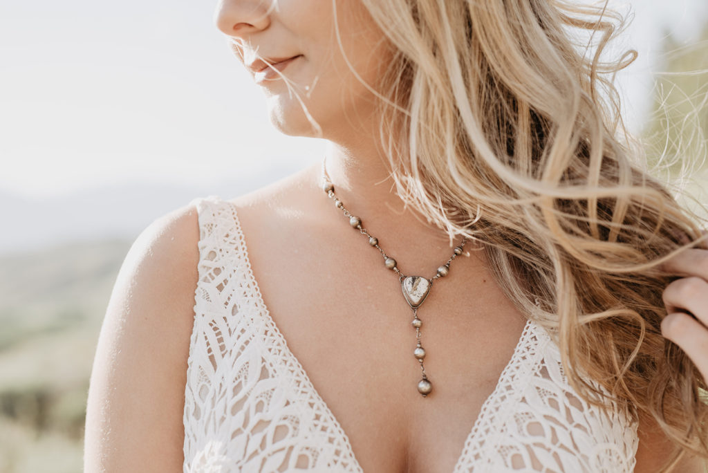 Jackson Hole photographer captures detail shot of brides necklace as her hair blows in the wind and the sun shines behind her for her Wyoming elopement