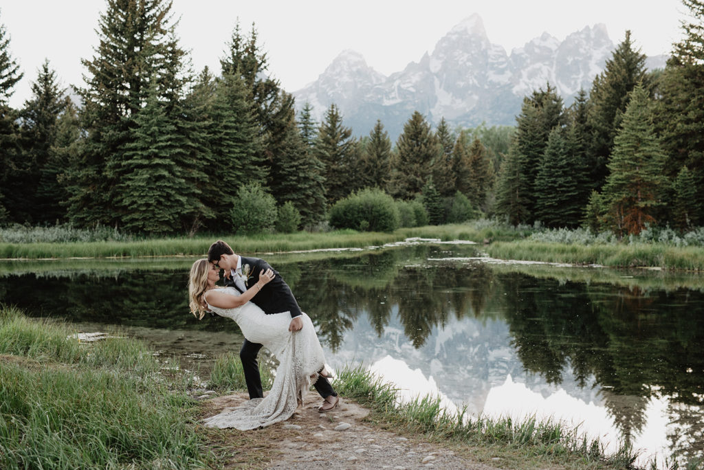 groom dipping his bride backwards at Schwabacher Landing with the Tetons in the distance captured by jackson hole wedding photographers