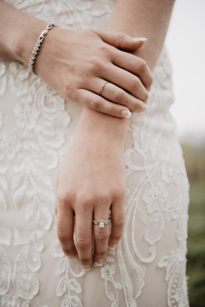 detail shot of an engagement ring as the bride holds her hand by the side of her lace gown