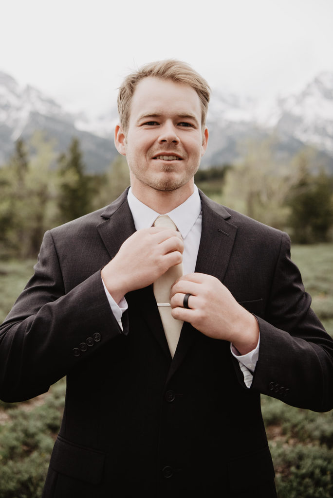 groom in a black suit adjusting his tie before his ceremony in the Tetons
